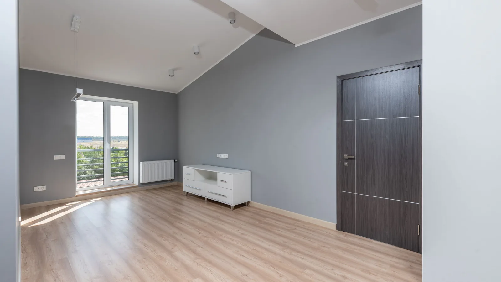 An empty room in a modern house, with light flooring, an open doorway and daylight along one wall.