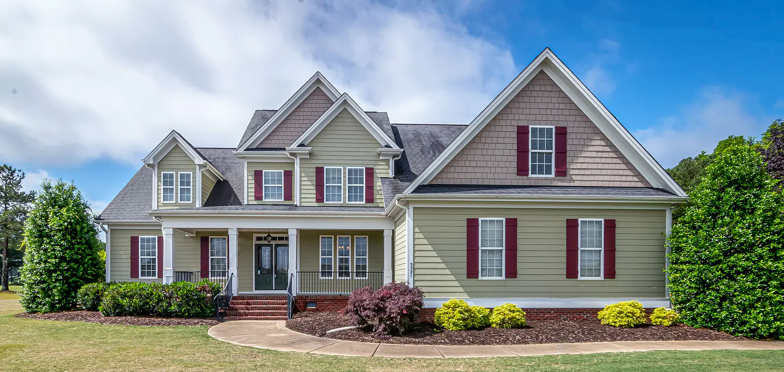 A two story suburban house with a covered porch and dark shutters, seen from the front lawn on a clear day.