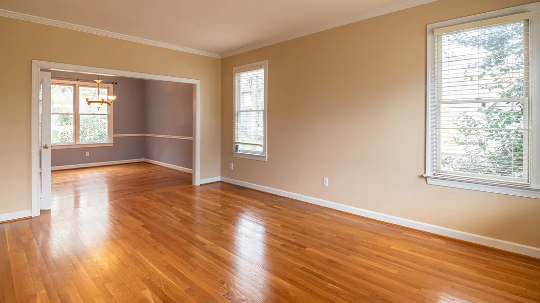 An empty living room with hardwood floors, painted walls and daylight through two windows.