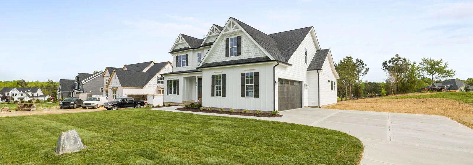 New suburban houses along a wide concrete driveway, seen across an open lawn.